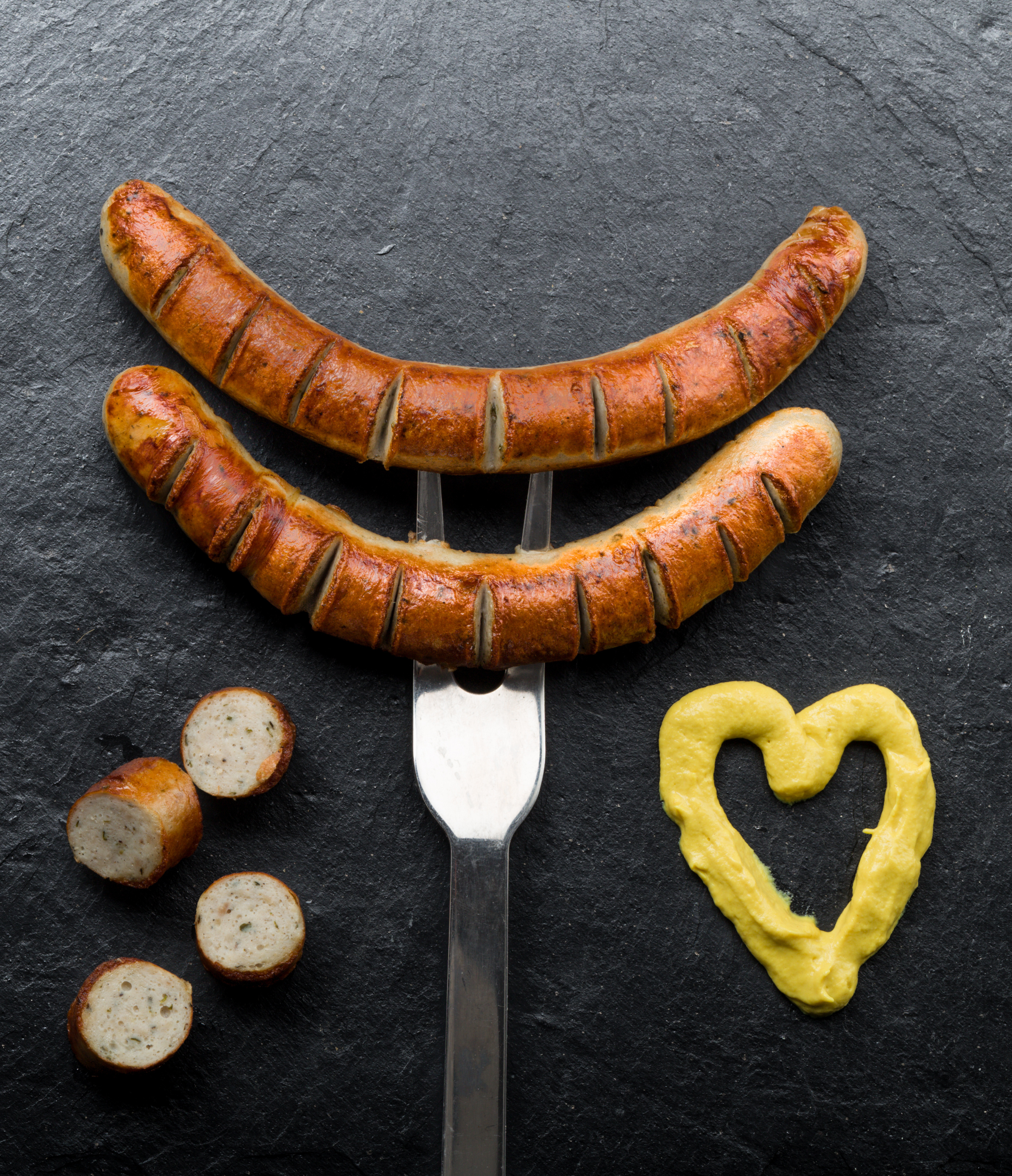 Zwei gebratene Würste auf einer Grillgabel.