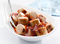 Einige Stücke gebratener und geschnittener Bratwurst mit Currysauce in einer Porzellanschale.